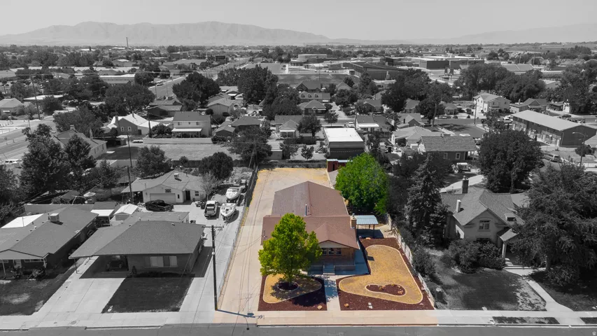 Single-story property with a brown roof, expansive paved drive, and a landscaped yard featuring decorative rock and mature trees