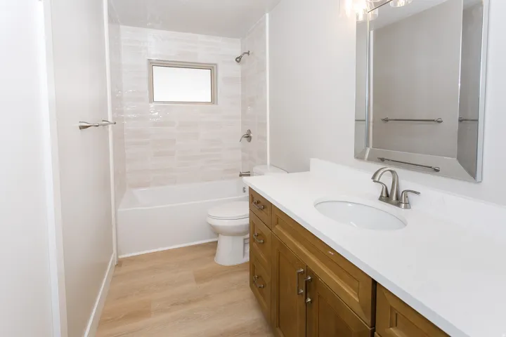 Wood-finish flooring, single vanity with a white countertop, recessed oval sink, and brushed nickel faucet