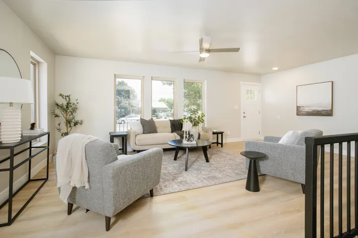 Bright living area featuring wood-finish flooring, multiple large windows, a ceiling fan, and a white paneled entry door