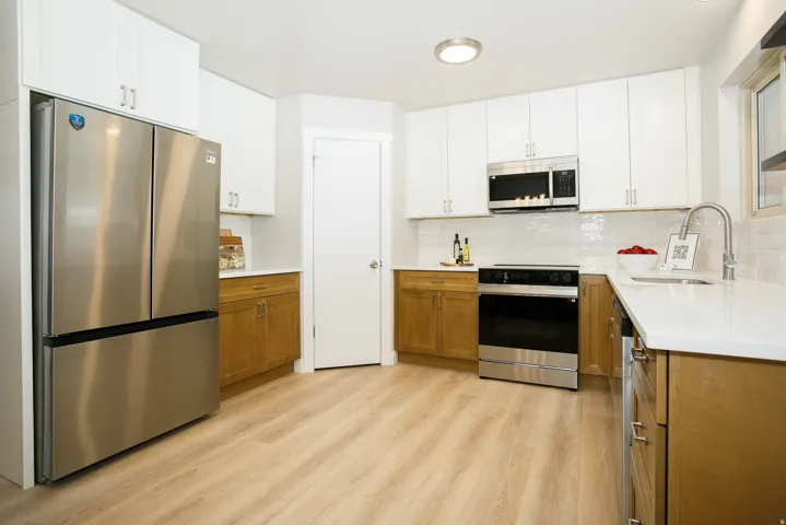 Updated kitchen featuring stainless steel appliances, white upper cabinetry, wood-finish lower cabinetry, white countertops, and wood-finish flooring