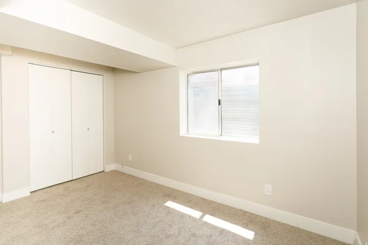 Neutral-toned carpeting, light-colored walls, white trim, sliding window, and bi-fold closet doors