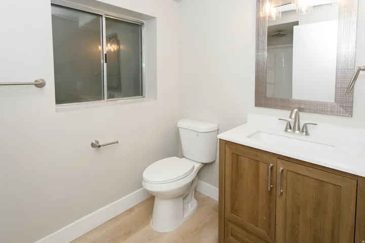 Bathroom featuring a wood-finish vanity with a white countertop, undermount sink, and a framed mirror