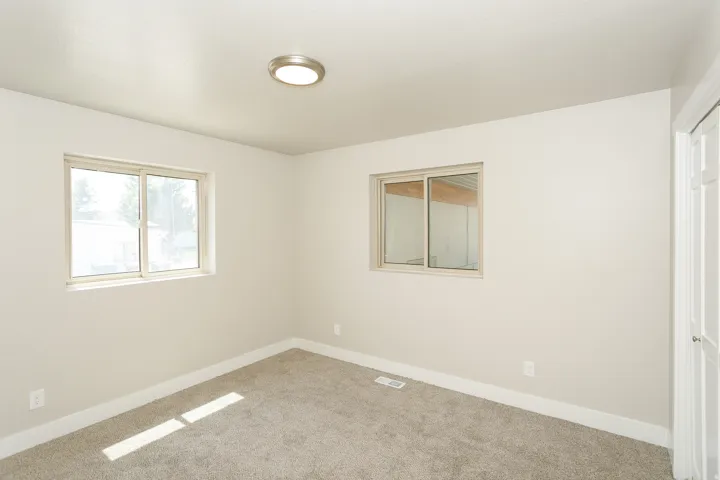 Neutral wall paint, plush carpet flooring, two windows, and flush-mount ceiling light