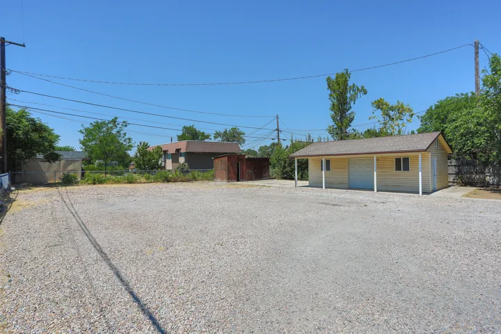 Gravel lot with an auxiliary building featuring horizontal siding, white trim, and a covered porch