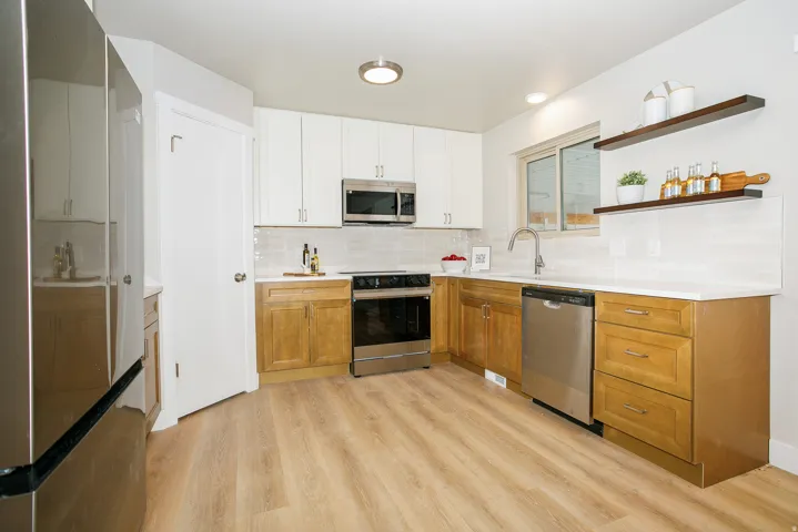 Kitchen featuring wood-finish flooring, two-tone cabinetry, stainless steel appliances, white countertops, and a tiled backsplash