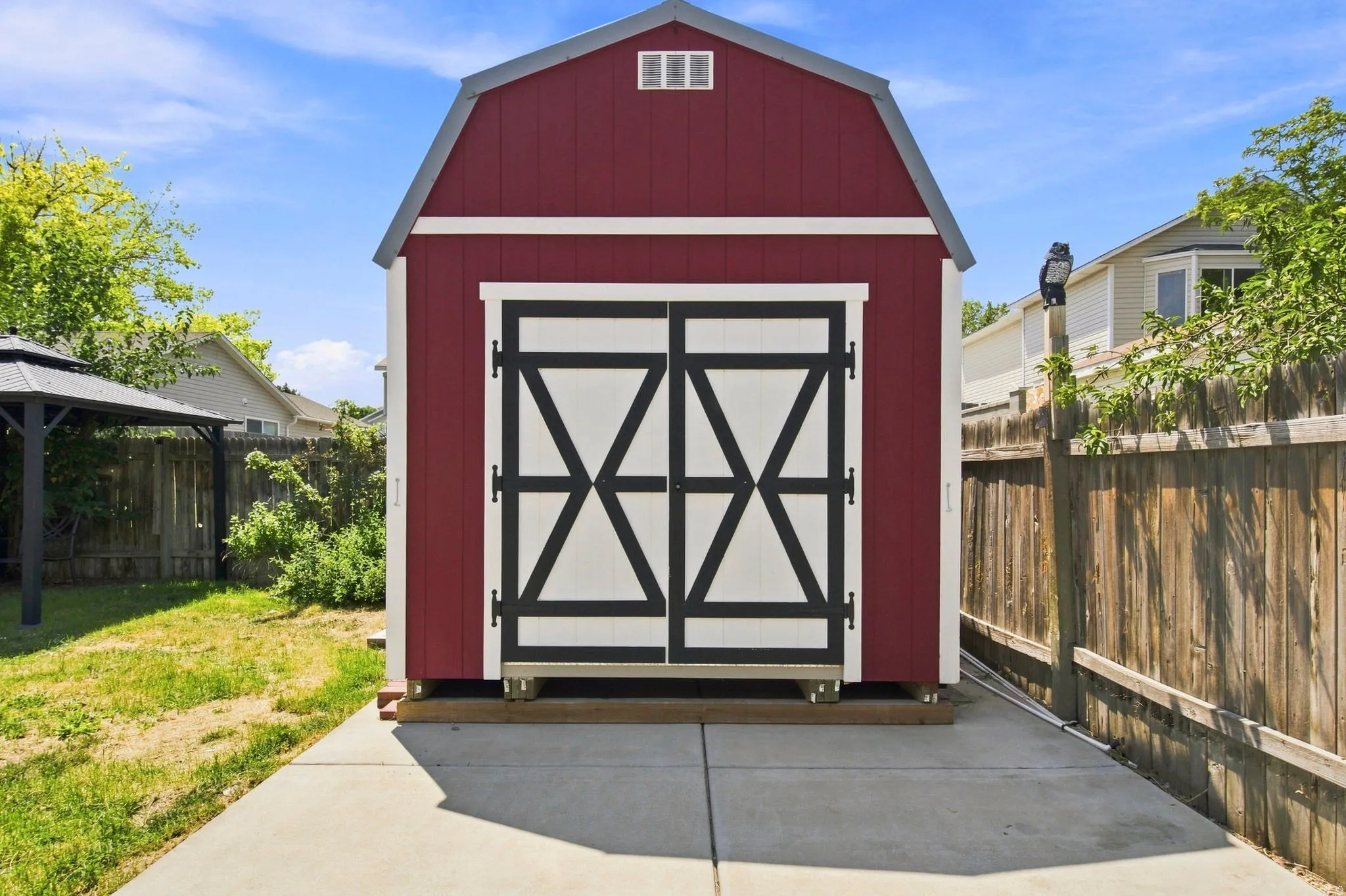 Red gable-roofed shed with white and black barn doors, set on a concrete pad