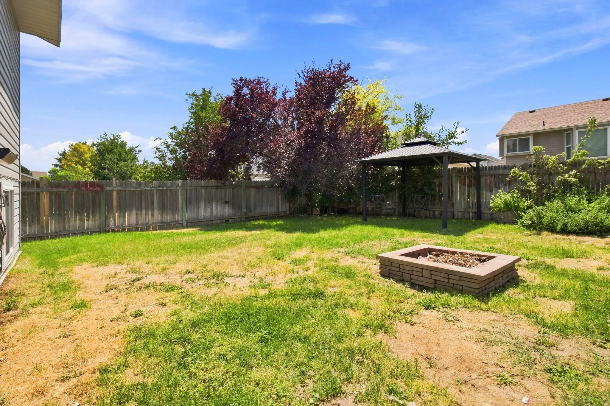Spacious fenced yard featuring a stone-look fire pit and a metal gazebo