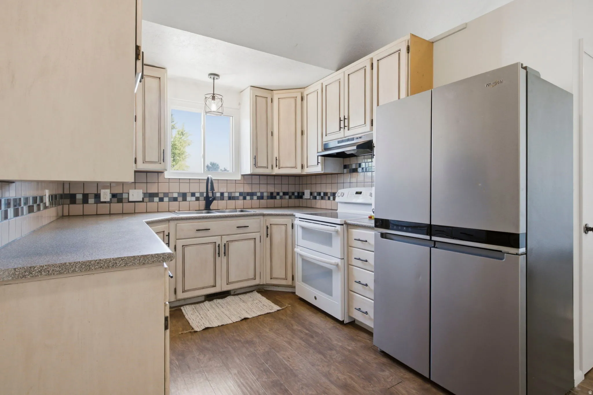 Kitchen featuring a stainless steel refrigerator, white electric range with double ovens, wood-finish flooring, and white cabinetry