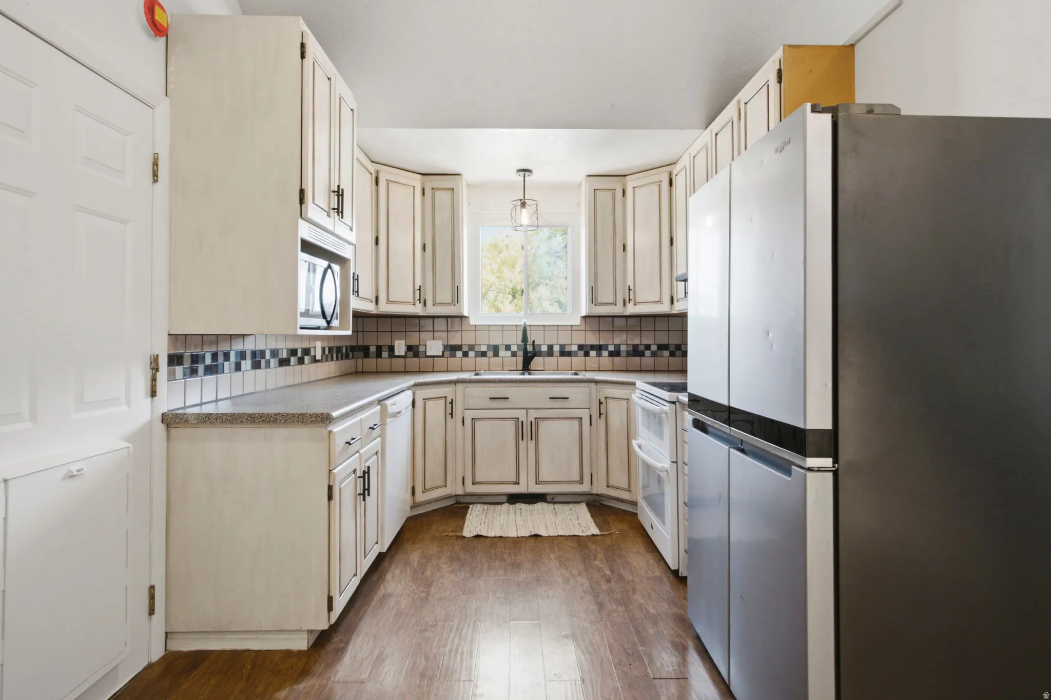 U-shaped kitchen with wood-finish flooring, light cabinetry, dark countertops, and a tile backsplash
