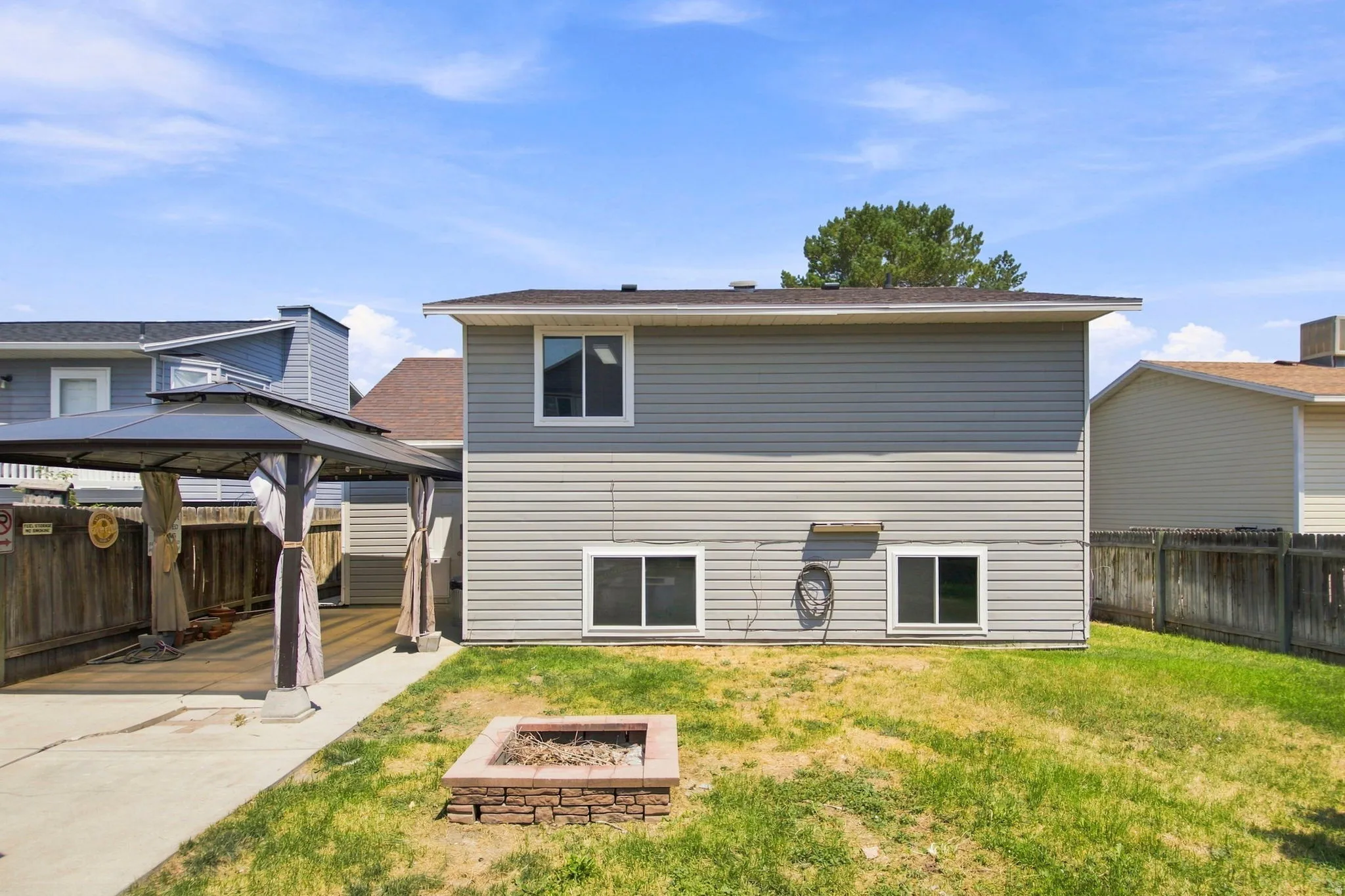 Rear exterior featuring horizontal siding, a ground-level patio, and a built-in stone fire pit