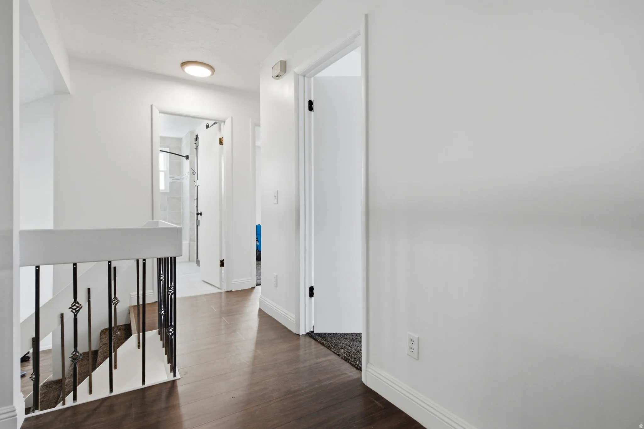 Hardwood-style flooring with white baseboards, a white painted staircase with black metal balusters, and a white interior door with black hardware