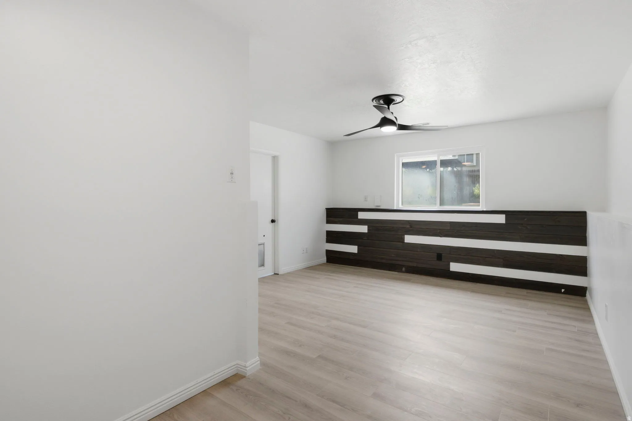 Wood-finish flooring, accent wall with horizontal paneling, modern ceiling fan, and recessed window
