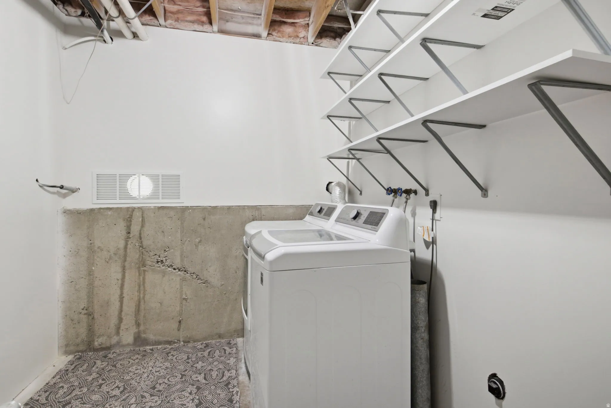 Laundry area featuring white walls, concrete foundation, and built-in shelving