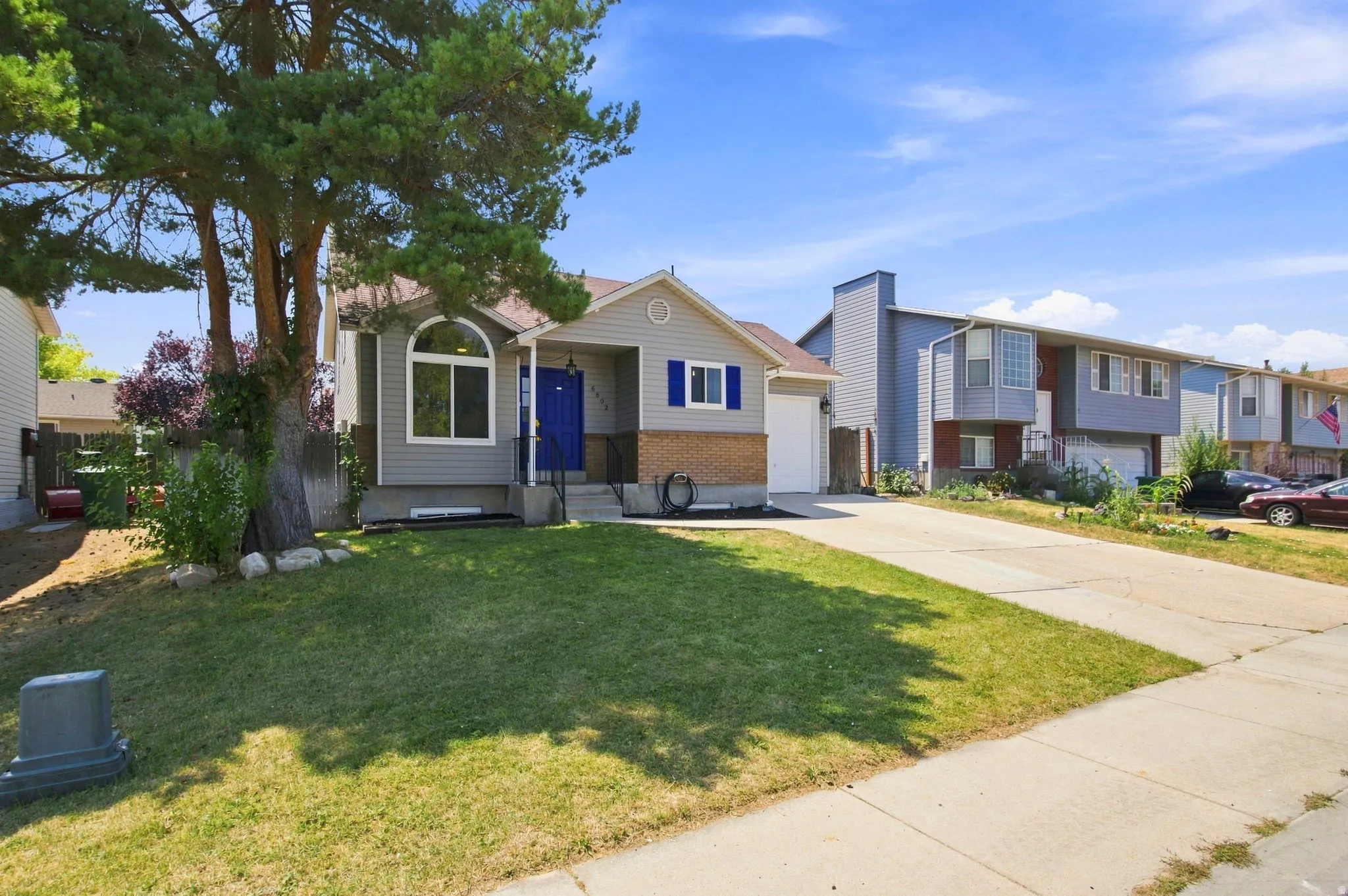 Single-story residence featuring a gray exterior with brick accents, an arched window, and a prominent blue front door
