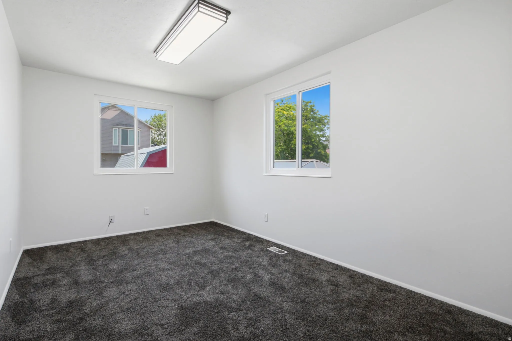 Neutral white wall paint, two pane windows, dark gray carpet, and a flush mount ceiling light fixture