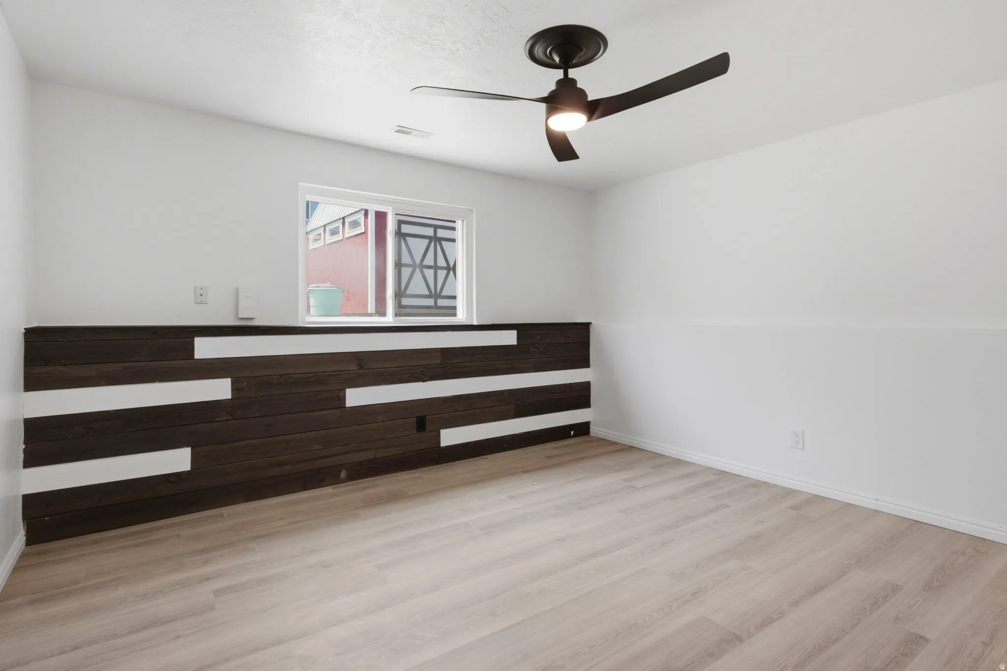 Laminate wood-finish flooring, accent wall with horizontal wood planks, recessed window, and ceiling fan with integrated lighting