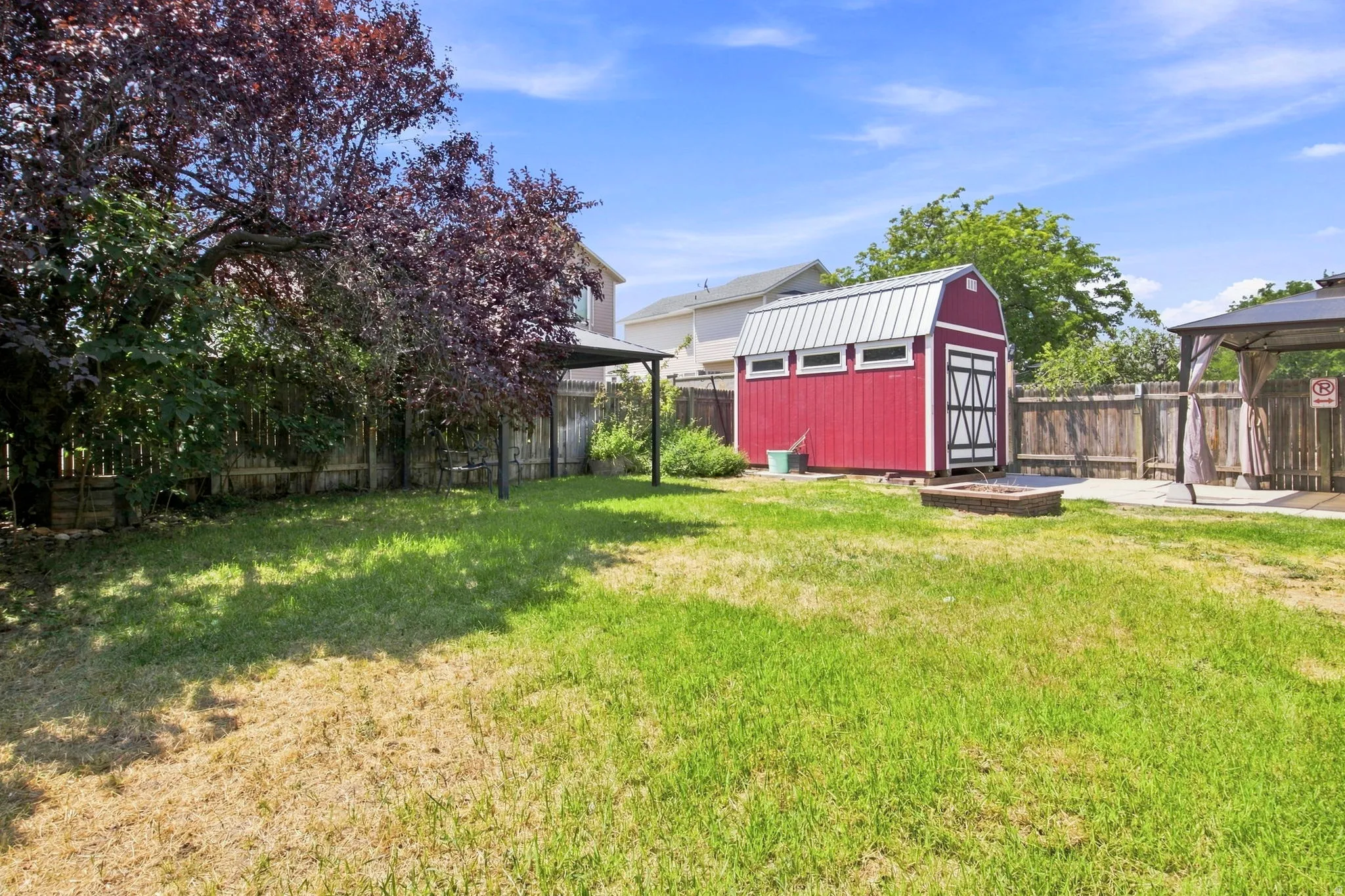 Expansive green space featuring a garden shed with a metal roof, partial privacy fencing, a covered pergola, and a concrete patio