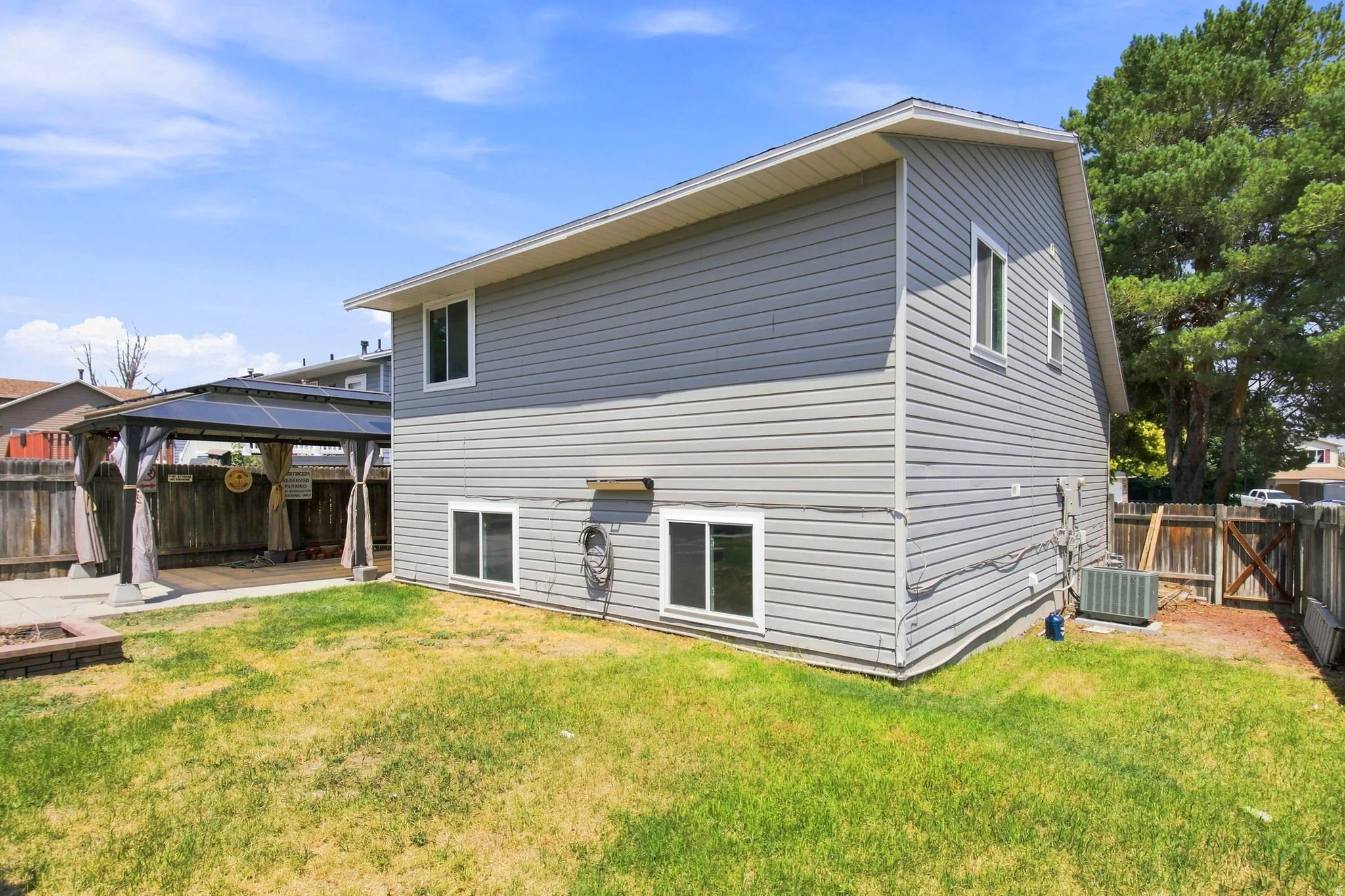 Two-story residence with gray horizontal siding, multiple windows, and a covered patio area