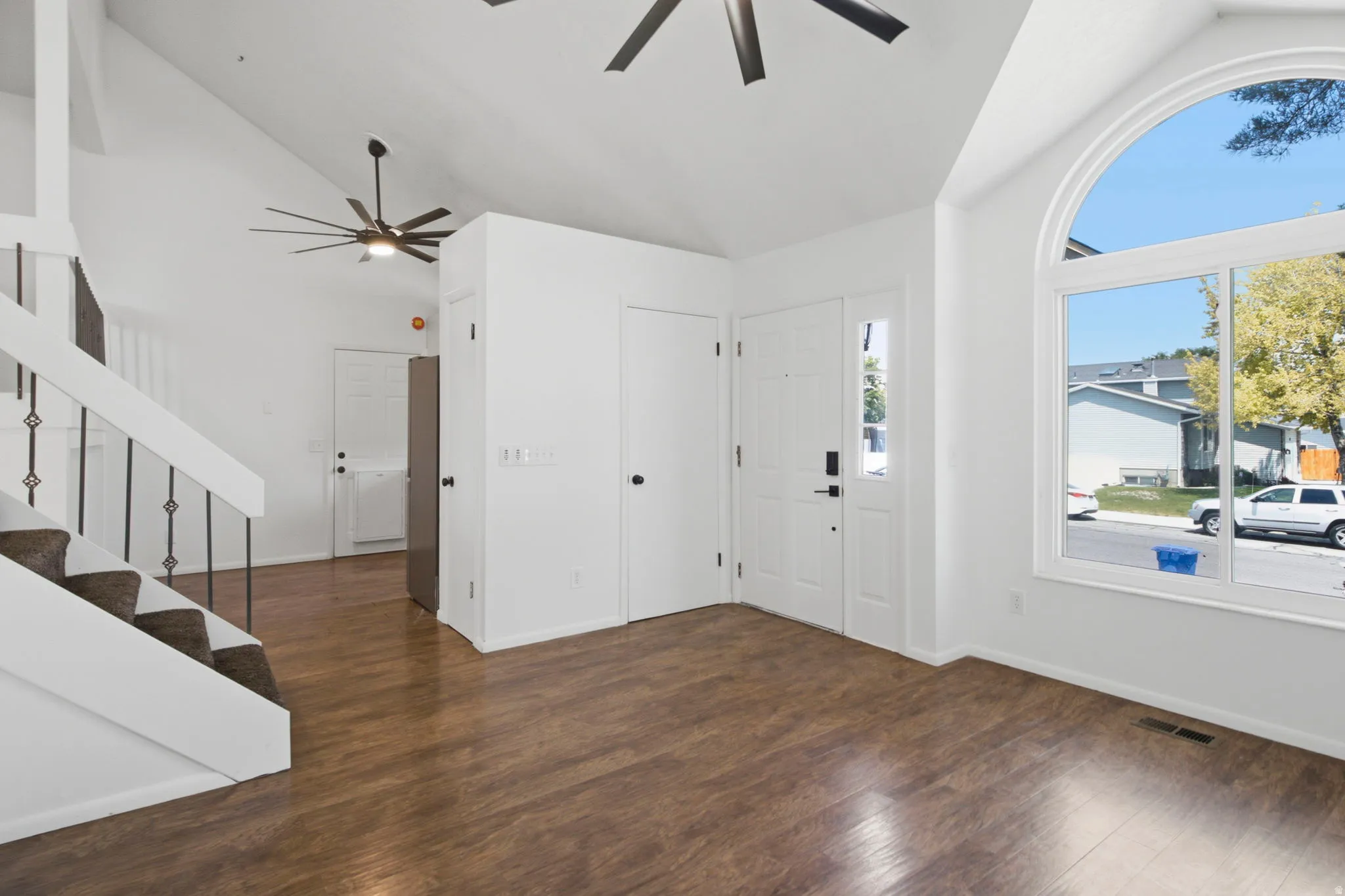 Vaulted ceilings, wood-finish flooring, staircase with metal balusters, arched top picture window, and a paneled front door with sidelight