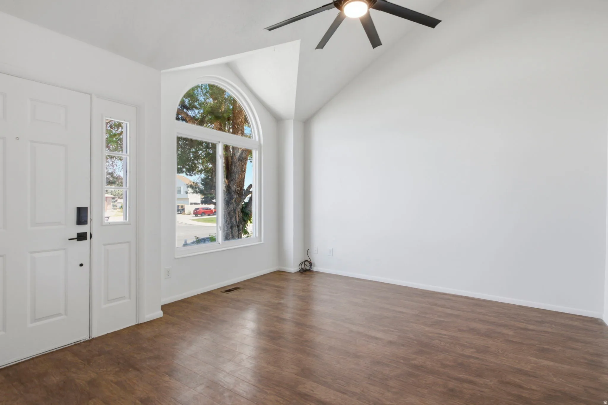 Vaulted ceiling with an attached ceiling fan, large arched window, wood-finish flooring, and a white paneled entry door with sidelight