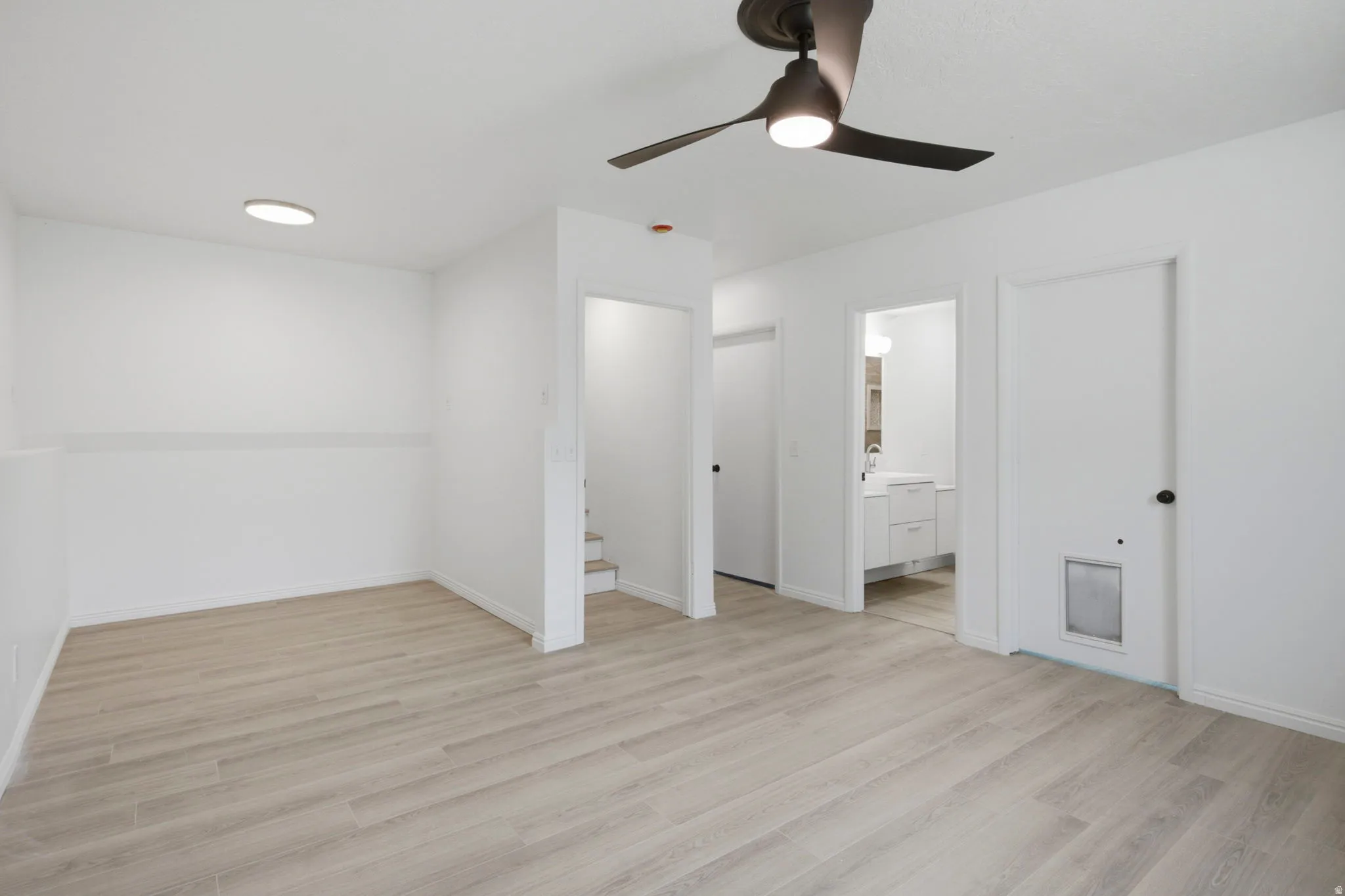 Smooth, light wood-finish flooring complements white walls, with a modern ceiling fan and recessed lighting providing illumination