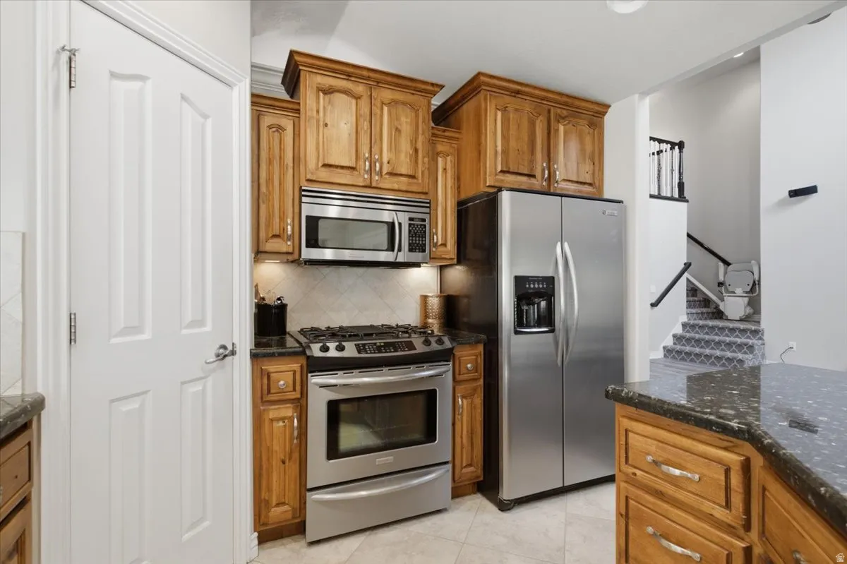 Wood-finish cabinetry, stainless steel appliances, granite countertops, tile backsplash, and light tile flooring
