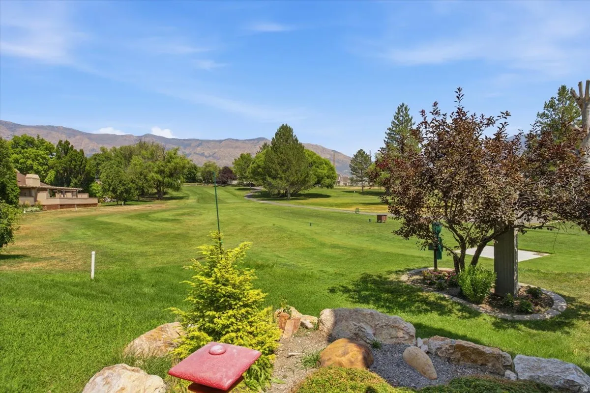 Expansive green space with distant mountain backdrop, mature trees, and a sculpted rock border