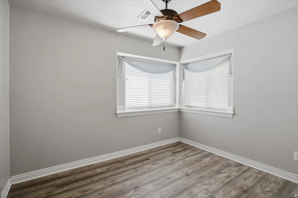 Wood-finish flooring, corner windows with blinds, ceiling fan with light fixture, and neutral wall paint