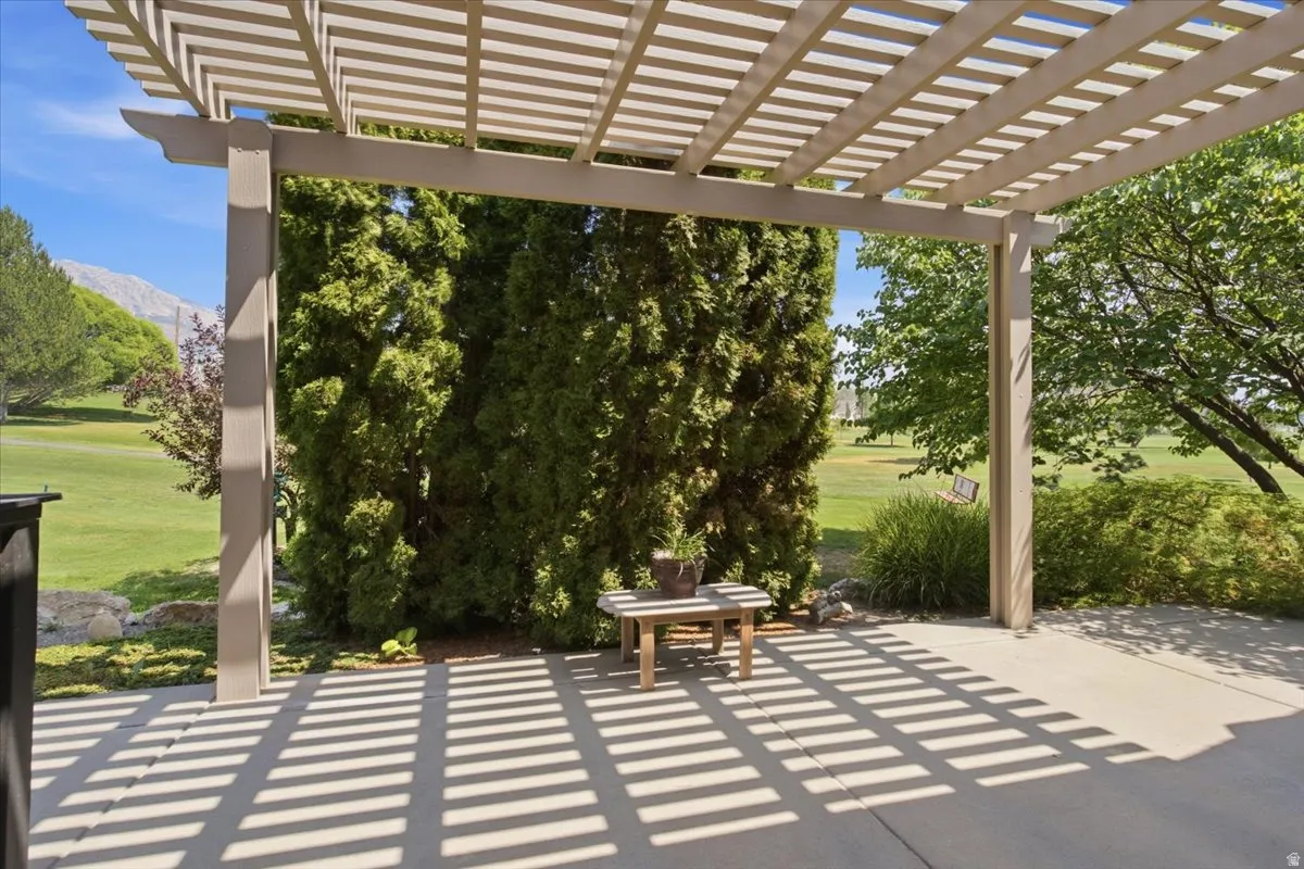 Pergola-covered concrete patio overlooking a manicured lawn with mature trees and distant mountains