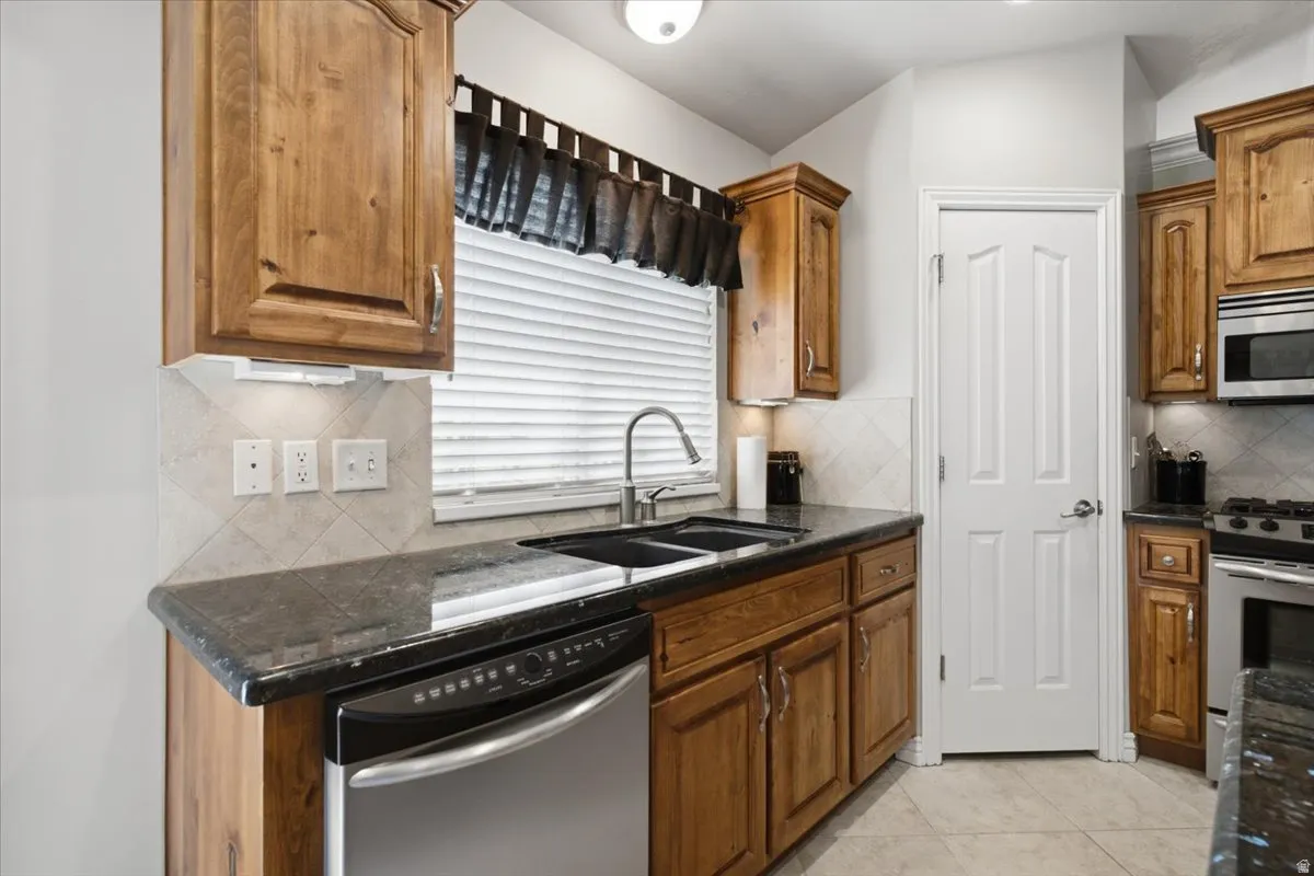 Kitchen with wood-finish cabinetry, dark countertops, a stainless steel dishwasher, and a tile backsplash