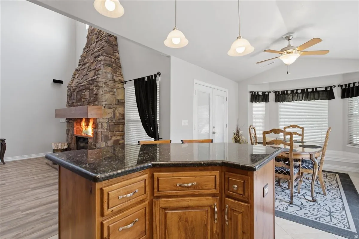 Stone fireplace with a wood mantel, wood-finish flooring, wood cabinetry, granite-finish countertops, and bay windows