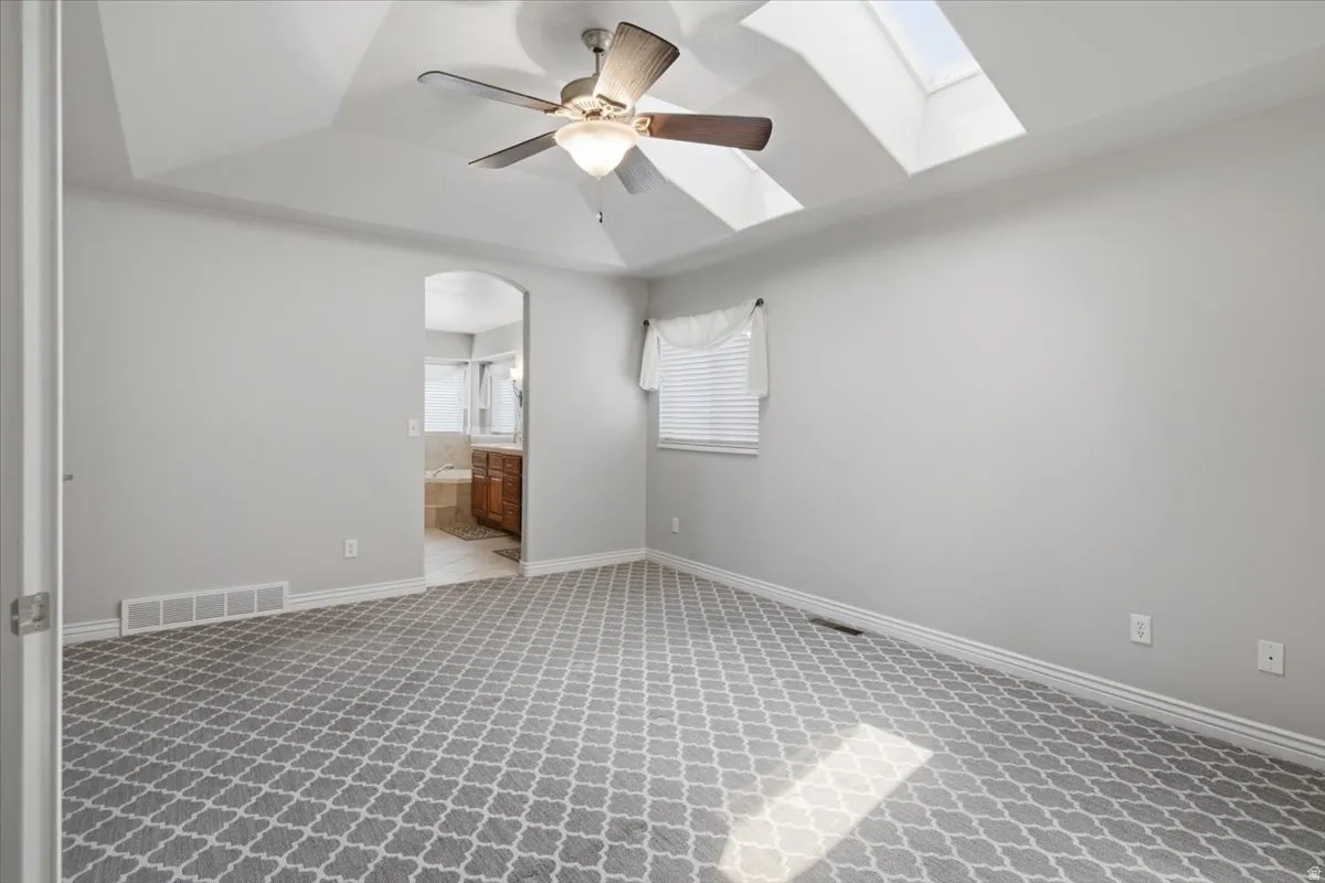 Vaulted ceiling with skylights, ceiling fan, and patterned carpeting