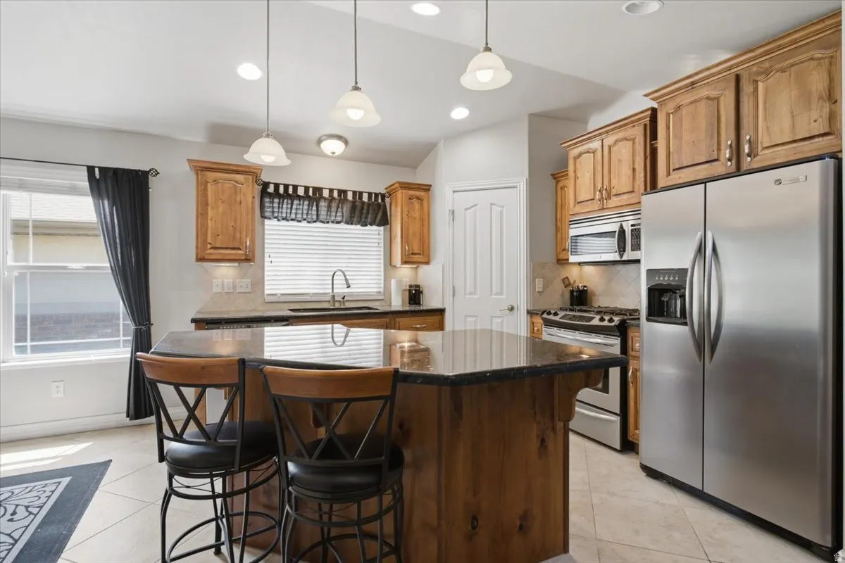 Kitchen featuring a central island, light wood-finish cabinetry, stainless steel appliances, pendant lighting, and tiled flooring