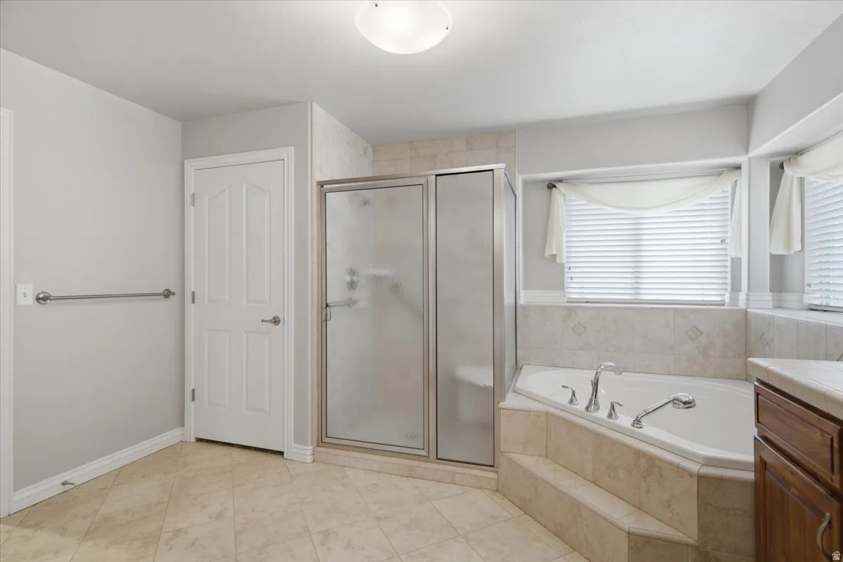 Spacious bathroom featuring a corner soaking tub, separate glass-enclosed shower, tiled flooring, and a vanity with a light-toned countertop