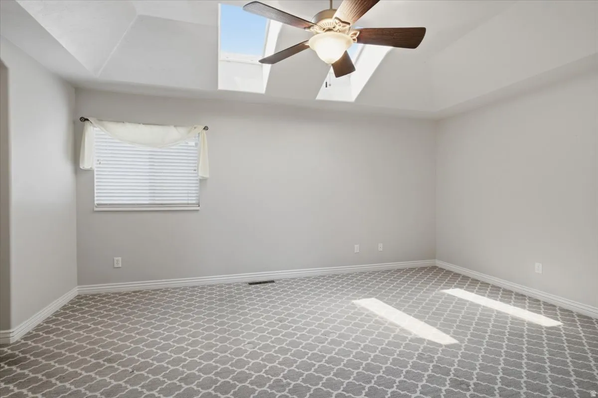 Tray ceiling with skylights, ceiling fan with light fixture, window with blinds, and patterned carpet flooring