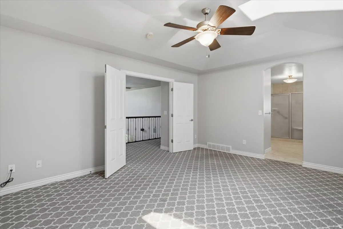 Spacious room with patterned carpet, a ceiling fan with integrated lighting, and white trim