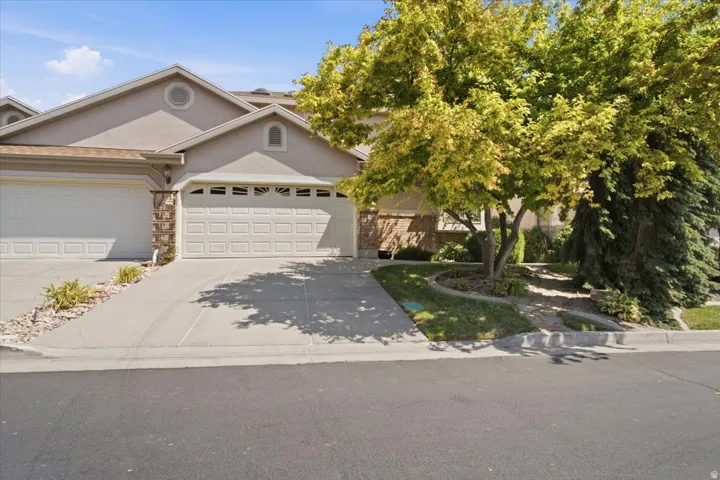 Stucco exterior featuring dual garage doors with decorative windows, a stone accent facade, and an arched entry above the garage