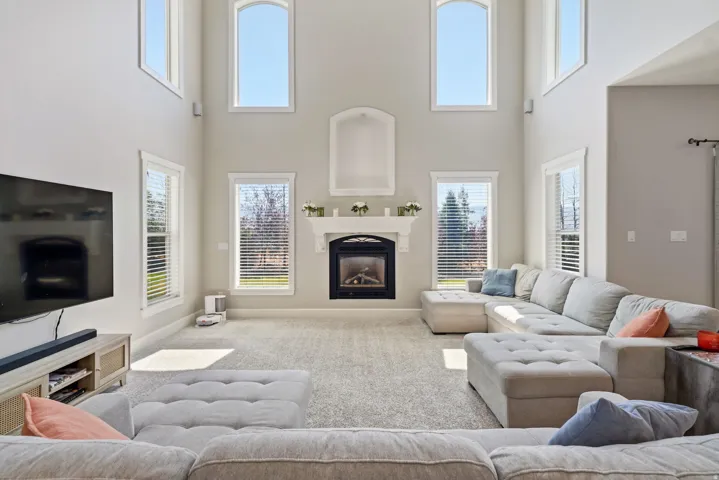 Two-story living area with a built-in fireplace, upper arched windows, and lower windows with blinds