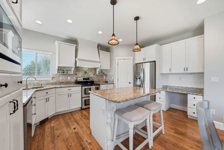 Kitchen featuring wood-finish flooring, white cabinetry, a built-in double oven, stainless steel appliances, and a central island with a stone-finish countertop