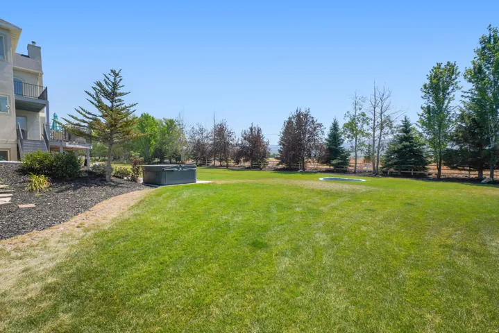 Expansive green lawn with a built-in hot tub, mature trees, and a terraced landscape featuring a mulched area