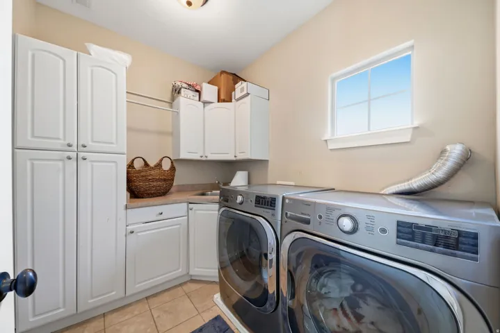 Integrated laundry space featuring white cabinetry, a built-in sink, and a window