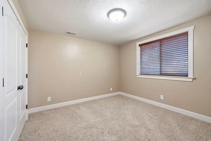 Wall-to-wall carpeting, window with blinds, overhead flush mount lighting, white trim, and a white interior door with dark hardware