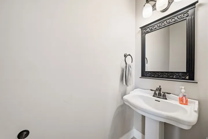 Pedestal sink with a bronze-finish faucet, framed mirror with ornate detailing, and wall-mounted lighting fixture