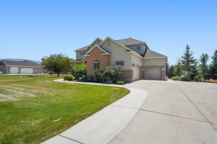 Two-story exterior with a brick and stucco finish, featuring a multi-car garage, mature landscaping, and an expansive concrete driveway