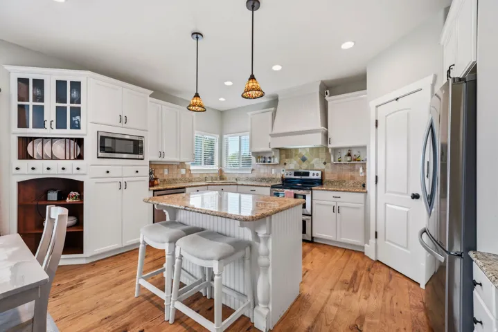 White cabinetry, granite countertops, wood-finish flooring, stainless steel appliances, and a kitchen island with pendant lighting