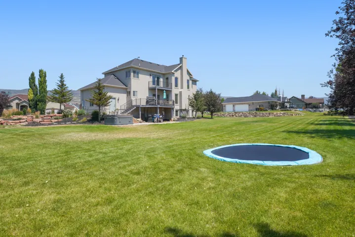 Expansive backyard featuring a manicured lawn, multi-level deck, and integrated hot tub