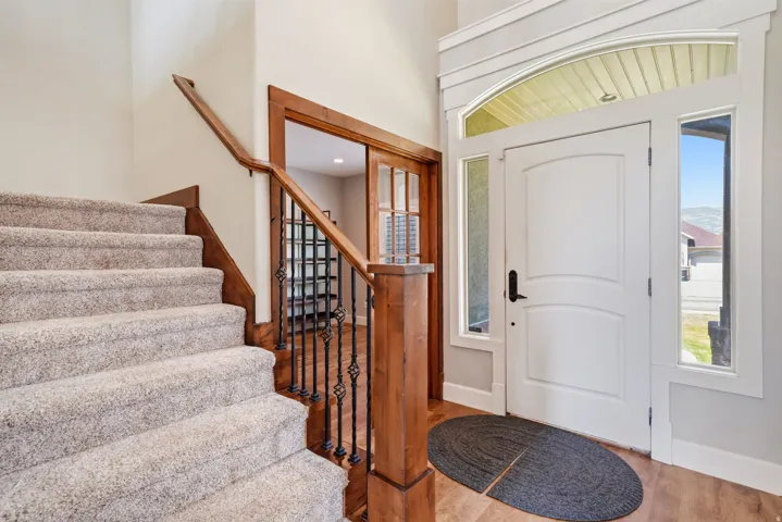 Entryway with wood-finish flooring, a white paneled door with sidelights and an arched transom, and a carpeted staircase with a wood handrail and wrought iron balusters