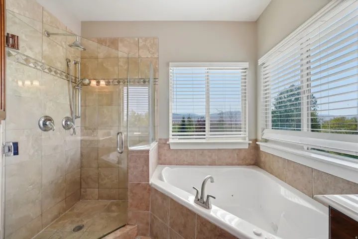 Tiled walk-in shower with glass enclosure, corner soaking tub, and dual windows