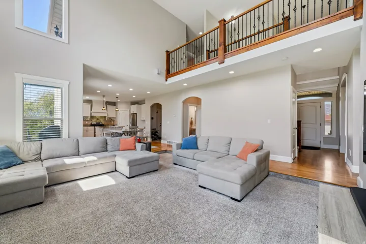 Two-story living area with a vaulted ceiling, recessed lighting, and a second-level wood and wrought iron railing
