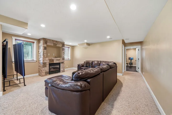 Carpeted living area featuring a stone-clad fireplace with a built-in media niche, recessed lighting, and multiple windows with blinds